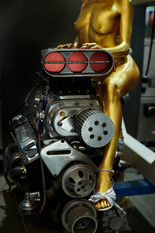Gold nude painted Goldfinger bond girl in an auto body shop sitting on supercharger big block Chevy Engine.