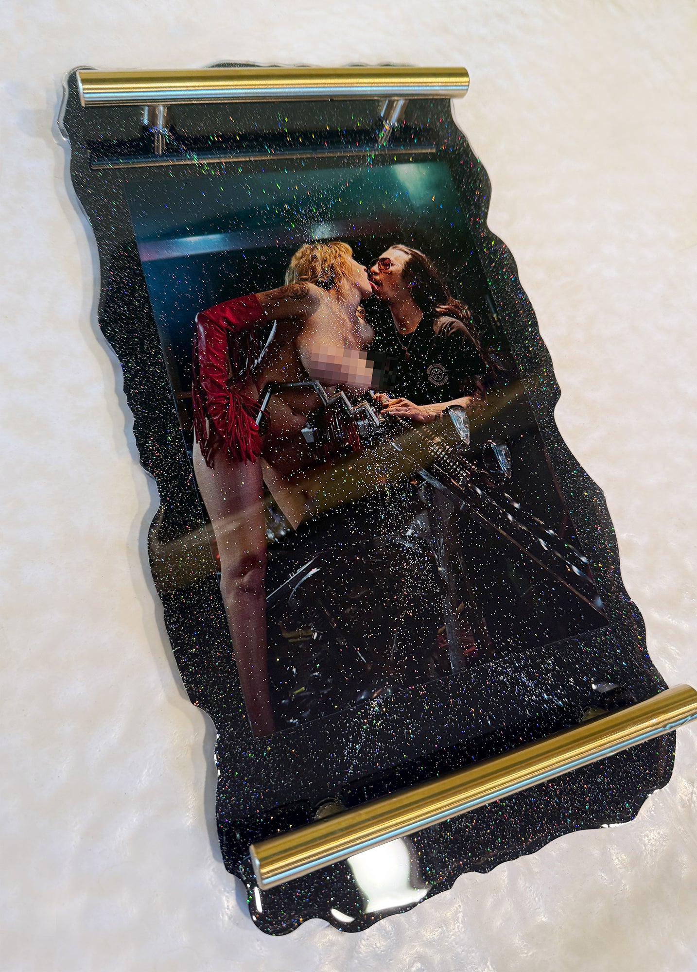 Metallic object with a reflective surface showing a couple embracing, placed on a textured white background.
