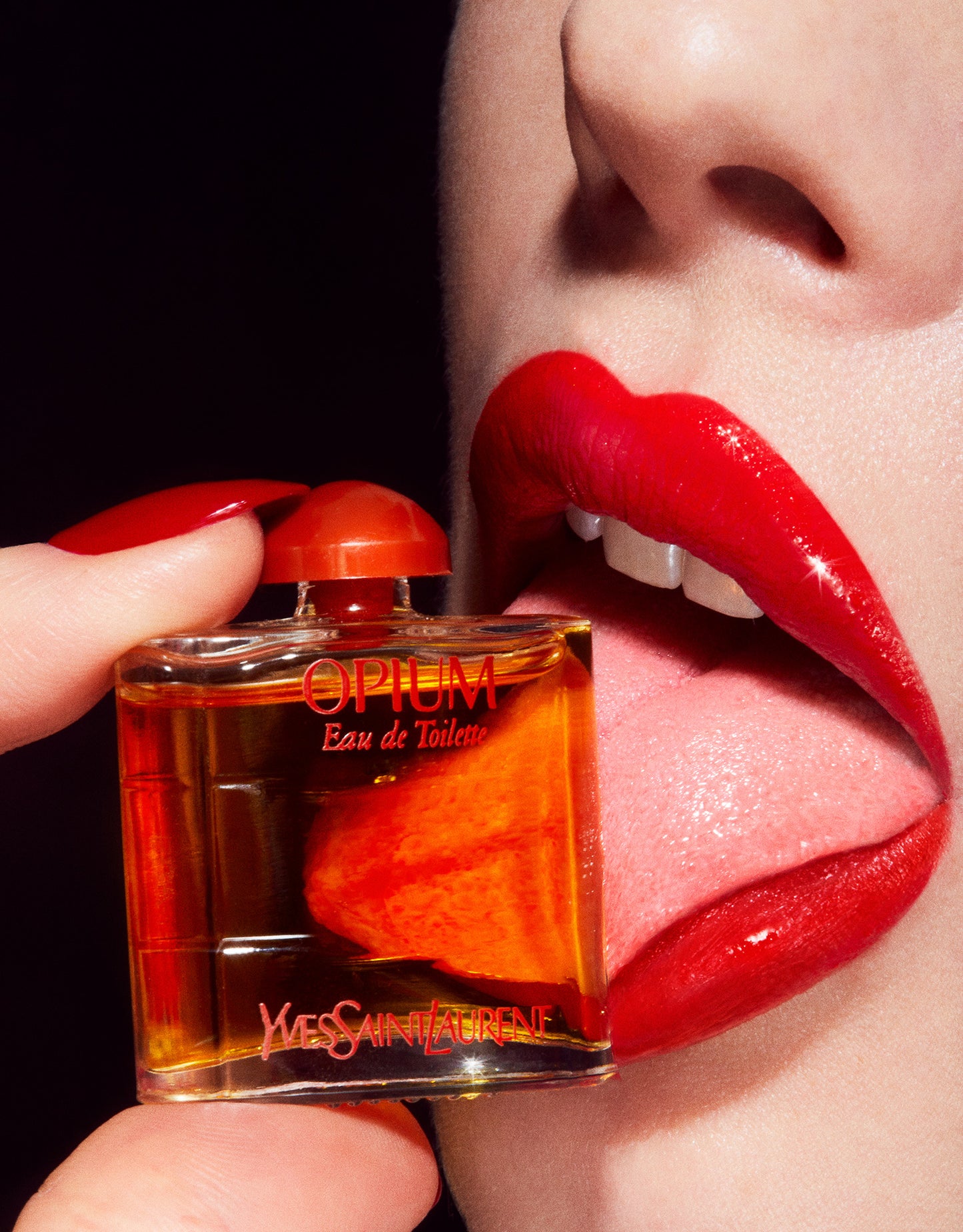 Close-up macro image of Woman with red glossy lipstick licking tiny dollhouse miniature opium yves saint laurent perfume bottle