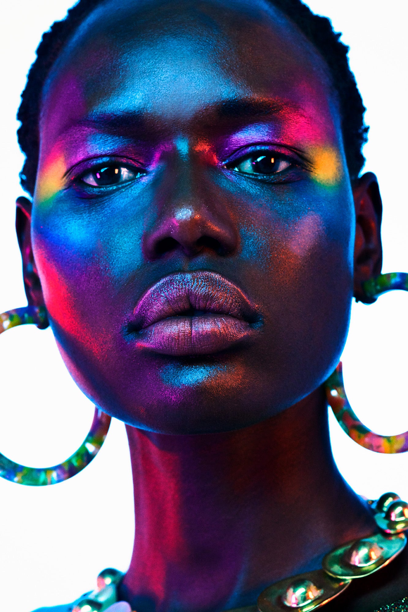 Black model wearing large 80s hoop earrings. Her face is covered with vibrant avant garde colorful rainbow festival makeup,