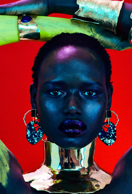 African model Ajak deng is covered in bracelets and earrings and wearing a large African gold neck ring extension style necklace.