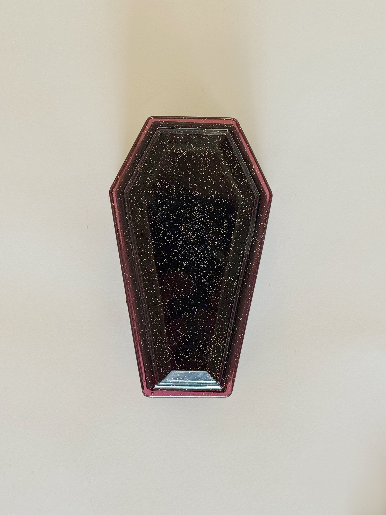 Coffin-shaped box with black glittery surface on a white wall