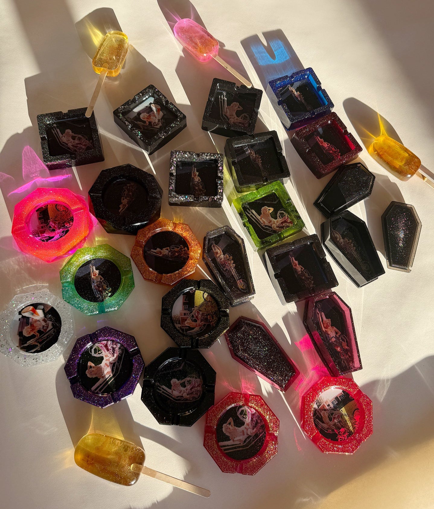 Assorted colorful resin lollipops and ashtrays with visible images on a white surface
