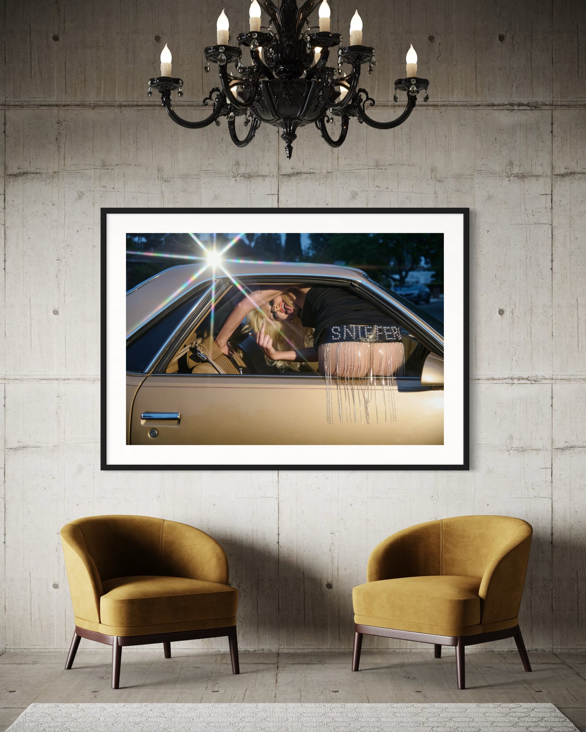 Framed artwork of a person in a car on a wall above two mustard chairs.