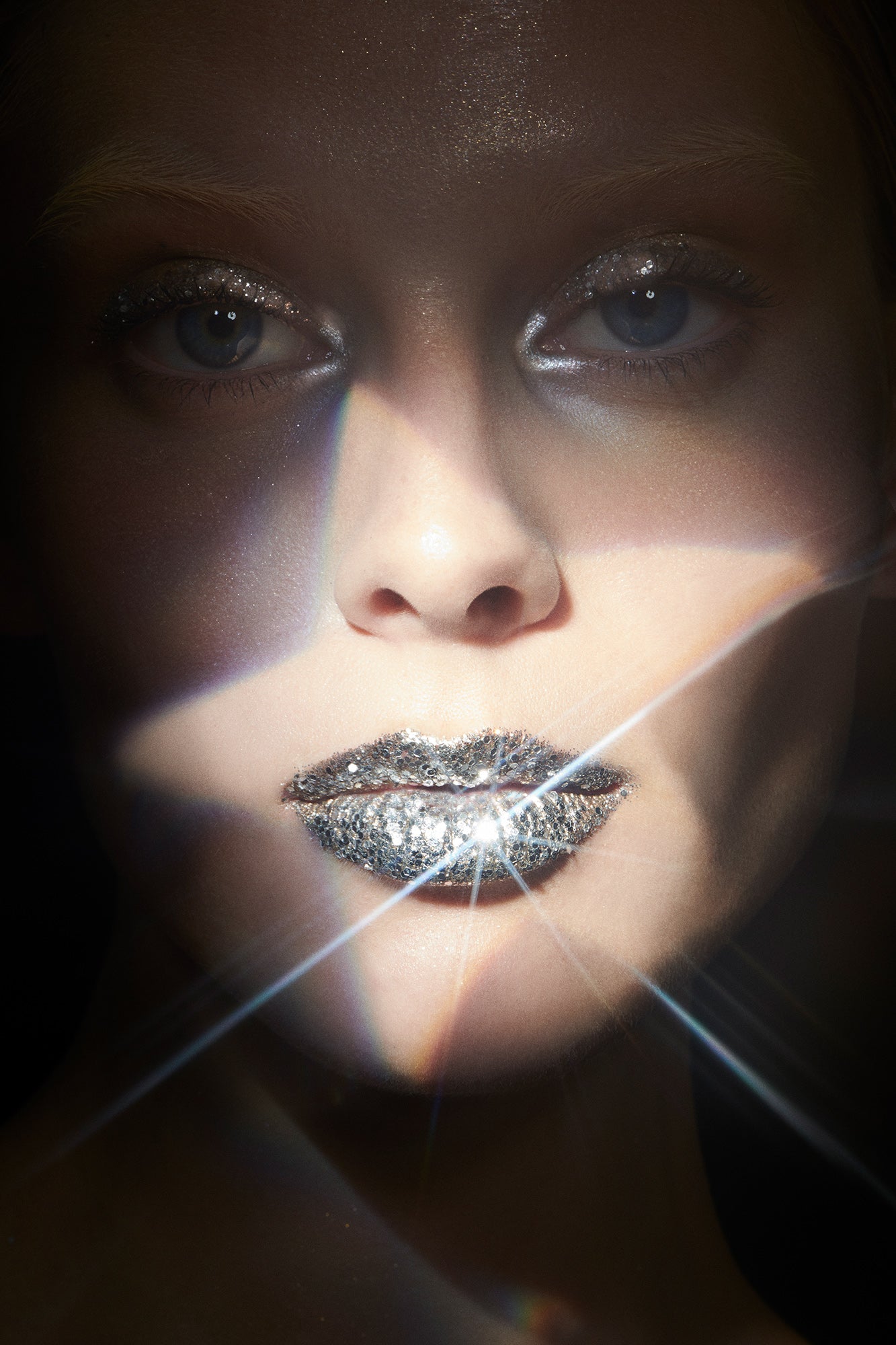 Beauty editorial of Woman in shadow wearing silver glitter eyeshadow and silver glitter lipstick with star light projected onto her face
