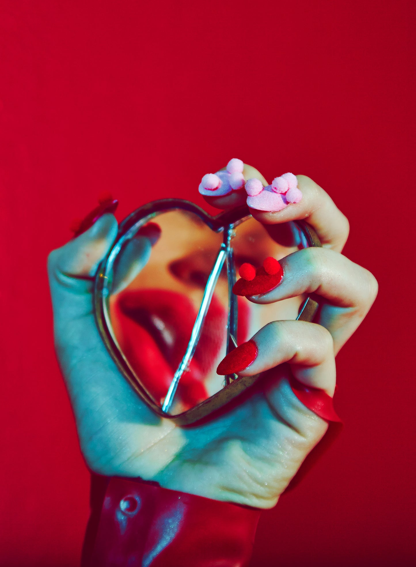 valentine's day love image of woman's hand with pom-pom nails manicure holding broken shattered heart mirror with lip reflection red background