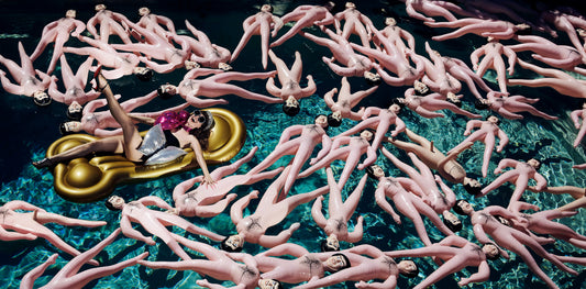 woman in pool surrounded by blow up men dolls and floating on a gold penis float wearing glamorous clothing shot by famous fashion photographer Jamie Nelson.