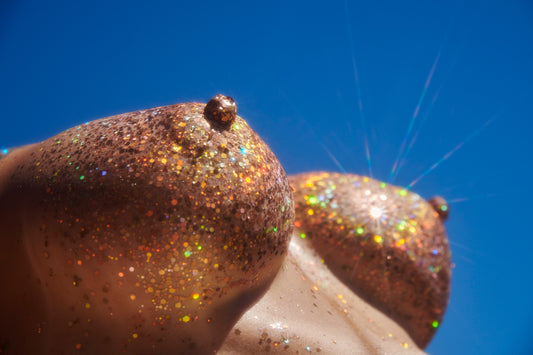 Close-up macro of boobs nipples covered in gold colorful glitter looking like mountain tops against blue sky glitter tit boob trend
