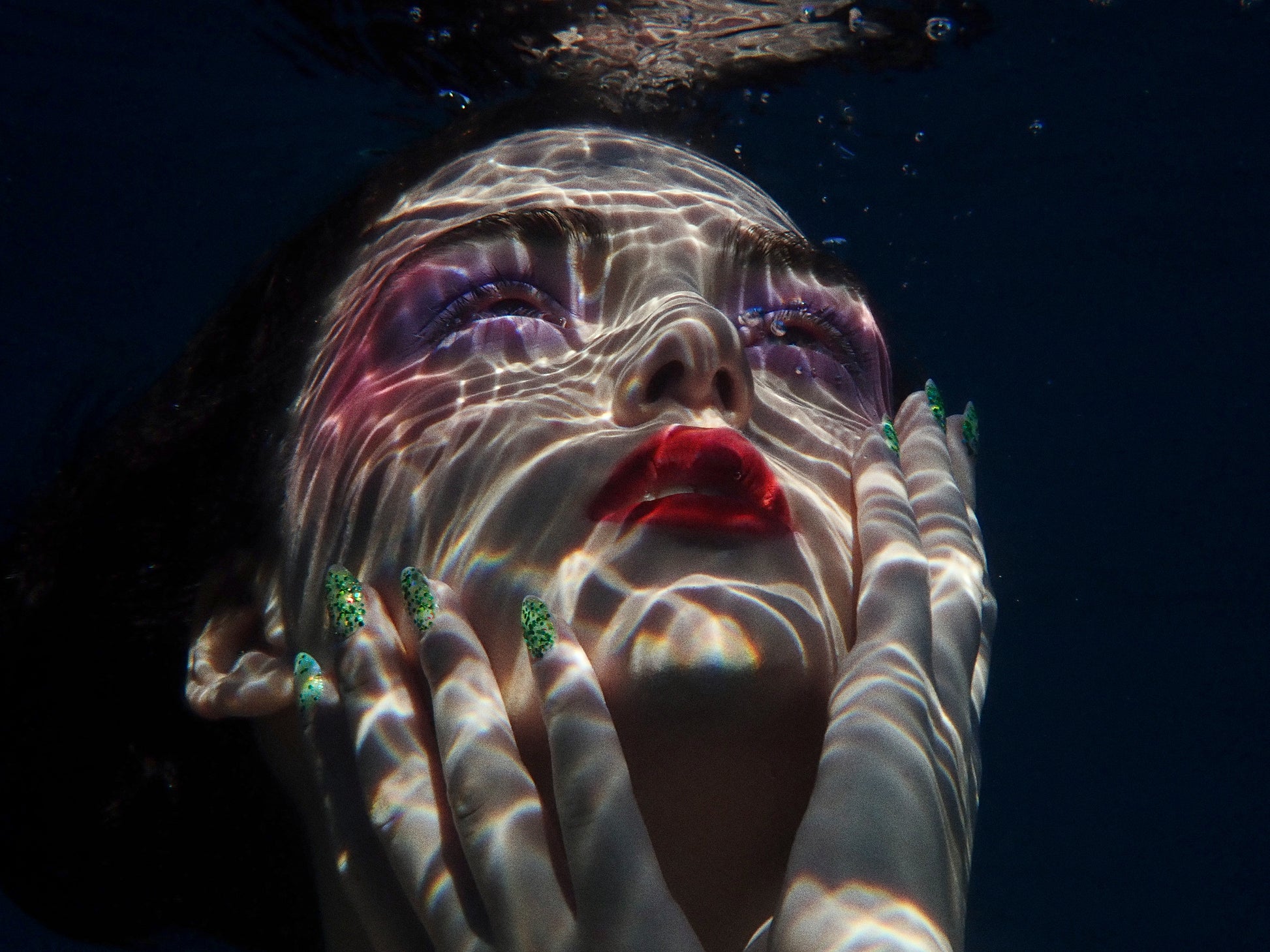 woman underwater with caustic reflections on face and creative colorful waterproof makeup