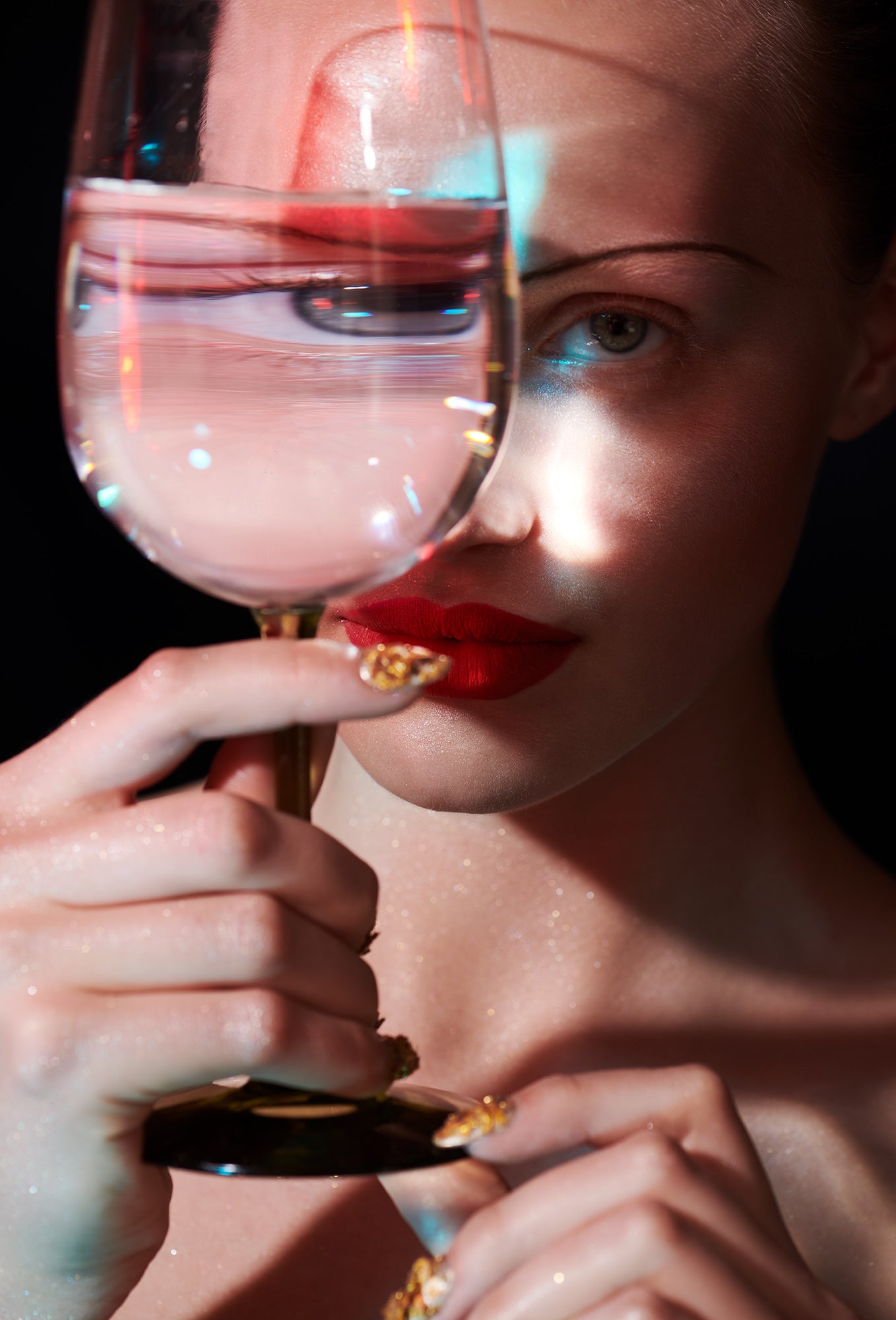 woman with red lips and thin pencil brows staring through a glass of water with big eye distortion