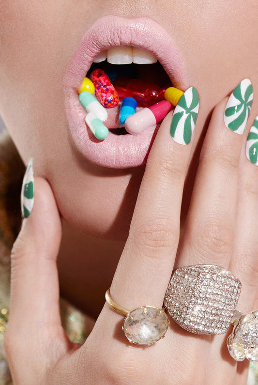 Close-up of vintage rings and pink lips as woman is popping colorful candy prescription pills drugs with psychedelic fingernails