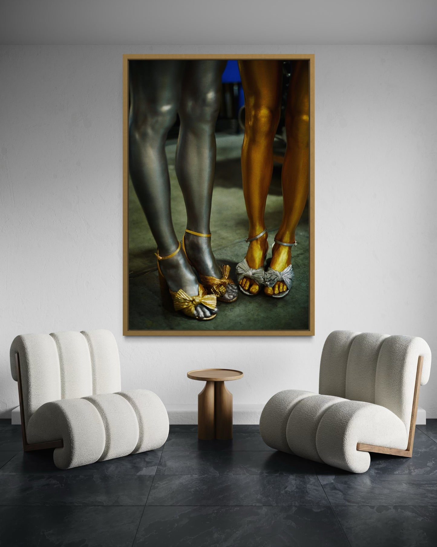 Framed artwork of women's legs and feet painted in gold and silver and wearing gold and silver shoes set in a modern interior with curved chairs and side table.