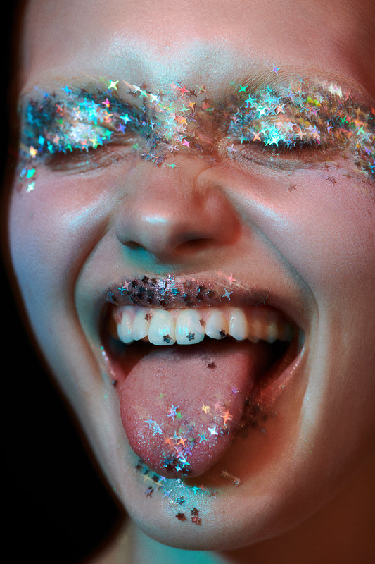 Woman covered in glitter eyeshadow and starry glitter on teeth laughing and celebrating new years holiday makeup trends