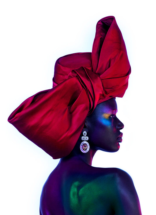 Portrait of black African woman with colorful makeup in side profile wearing giant red bow luxury hat and fine jewelry earrings. She is wearing a hat that is on theme for Christmas, a new year's party or celebration.