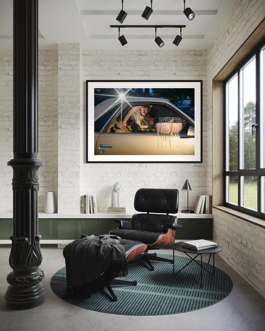 Modern interior with a black chair, rug, and framed picture on a white wall.