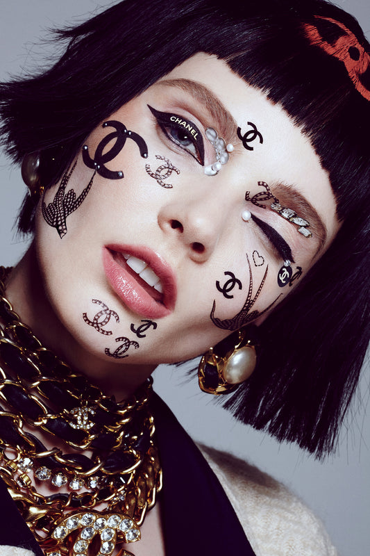 Woman winking covered in designer Chanel branded face stickers and tattoos and hair stencils.