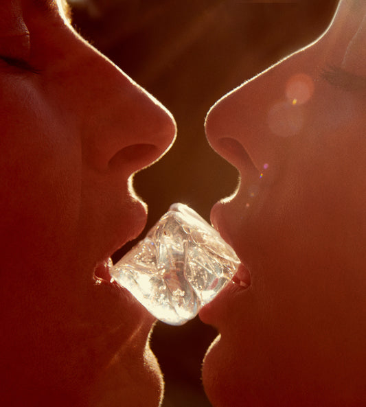 Close-up of two girls lips kiss with ice between them shot by famous female beauty photographer Jamie Nelson.