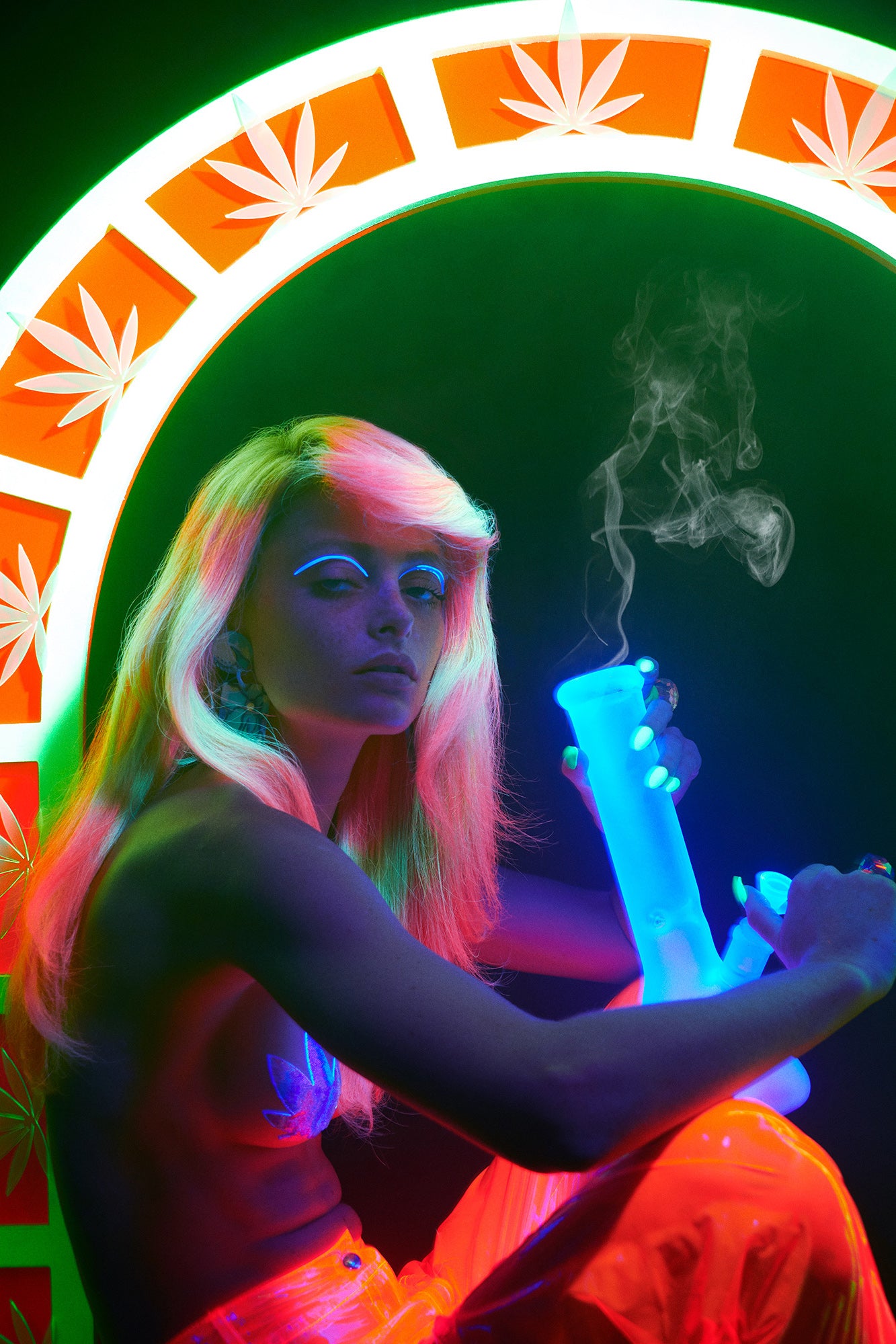 Glow-in-the-dark blacklight fashion editorial of Woman girl with neon green and pink hair and neon orange pants sitting under pot leaf decorated neon arch. She has a stoner expression squinted eyes as she lights up a bong.