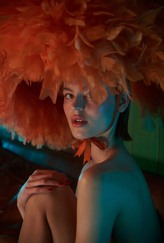 Person wearing a large orange feathered headpiece against a dark background