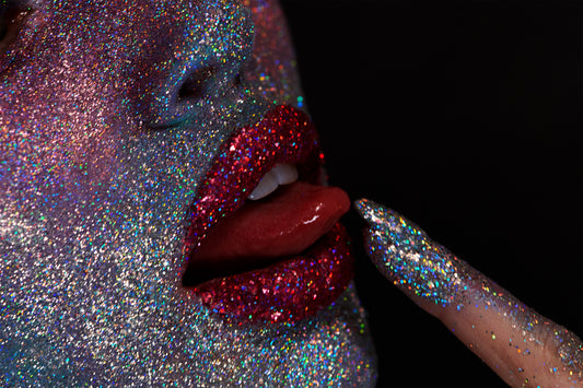 close up of woman's face covered in silver glitter avant-garde iridescent makeup and ruby slipper crystal lips as her tongue tastes licks glitter finger