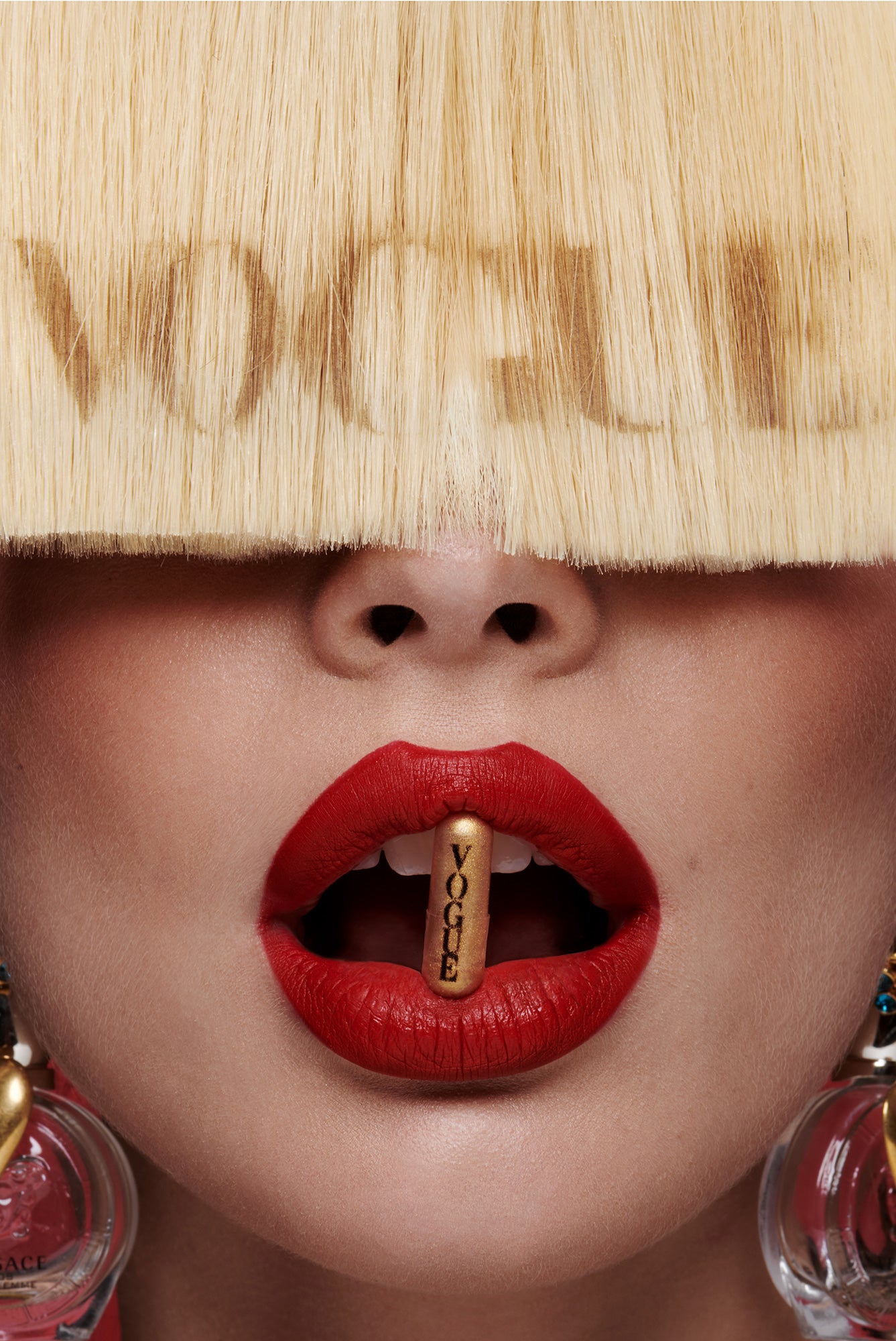 Glamorous Woman with red lipstick and large 80s bobble earrings with the word vogue stenciled in her hair and a gold vogue pill in her mouth