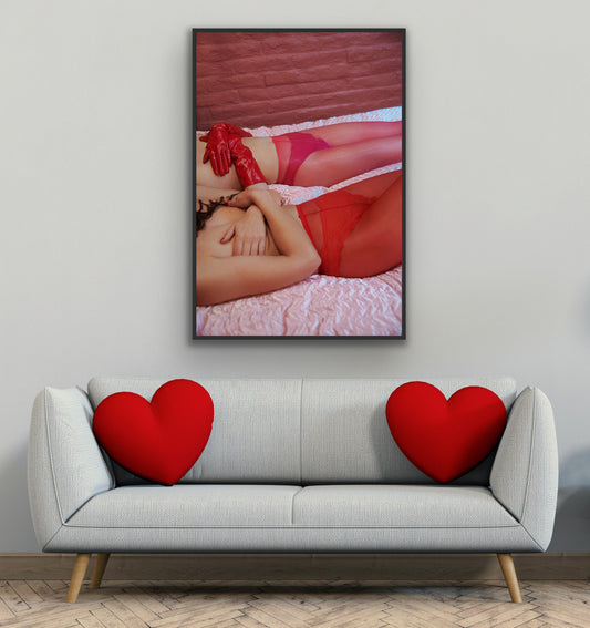 Framed artwork of a person in red lingerie on a wall above a gray sofa with heart-shaped cushions.