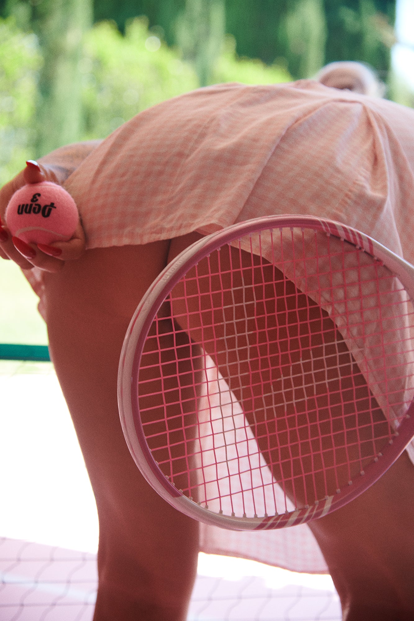 Woman in short pink tennis skirt bending over to serve tennis ball with her naked butt showing.