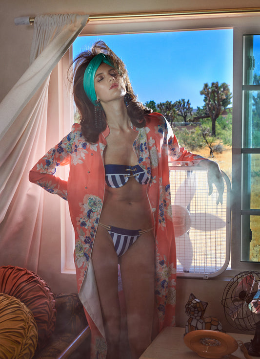 Person wearing a colorful kimono and striped bikini in front of a window with a desert view.