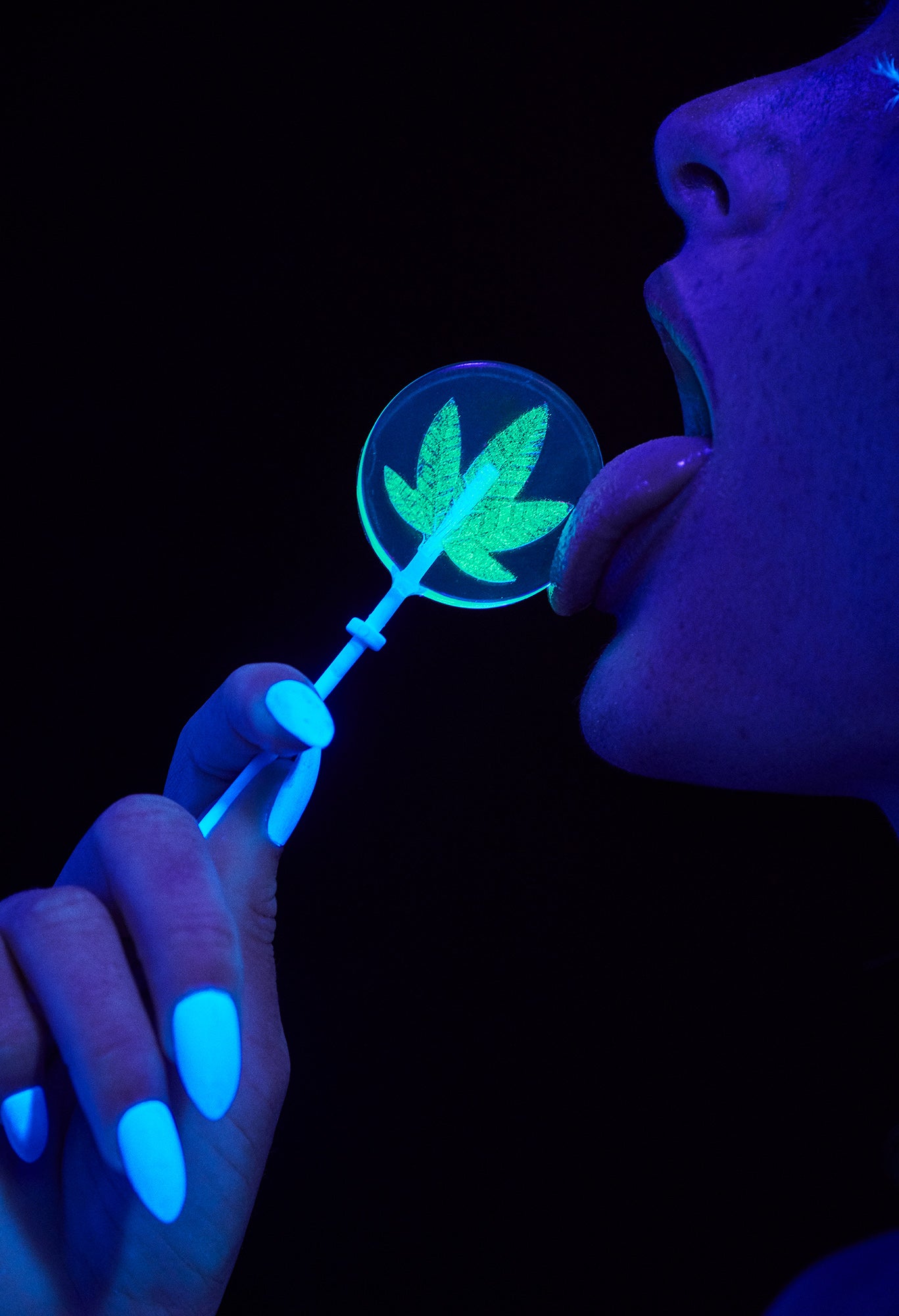 Blacklight fine art photography of girl with freckles licking neon glow in the dark weed lollipop cannabis sucker