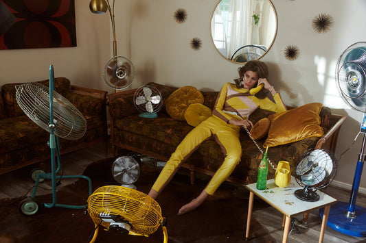 Person in yellow outfit lounging on a couch with various fans around
