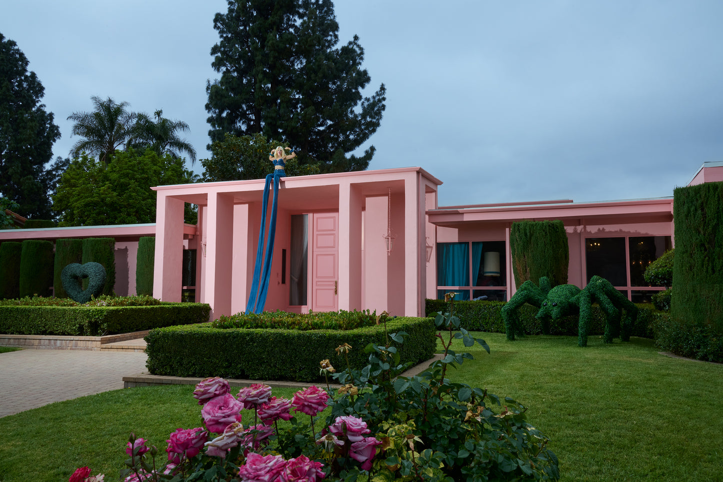 woman on top of Pink building wearing 20 foot long blue jeans with a garden and flowers in the foreground
