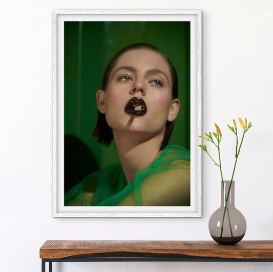 Framed artwork of a person with dark lipstick on a wall above a wooden shelf with a vase.