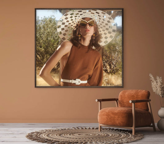 Framed artwork of a woman in a checkered hat on a brown wall above an orange armchair.