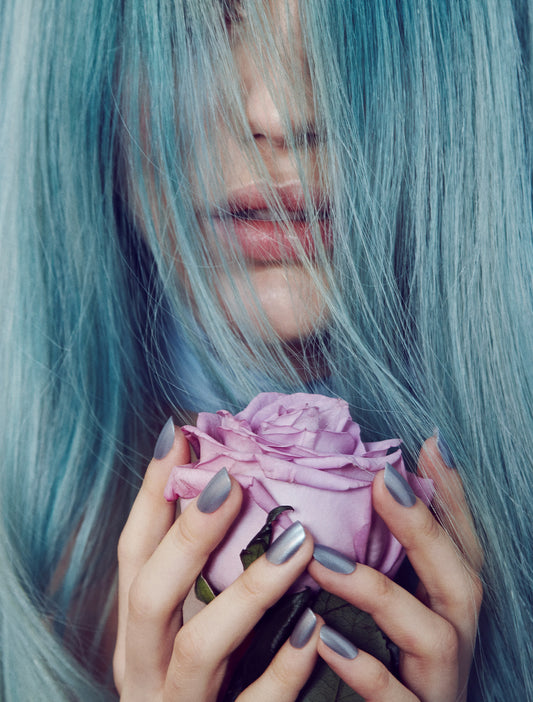 A artistic photograph of a woman with blue hair holding a purple rose, with a focus on her hands and the rose.