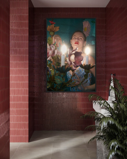 Artistic wall piece with a woman's face surrounded by plants and candles in a room with red brick walls.