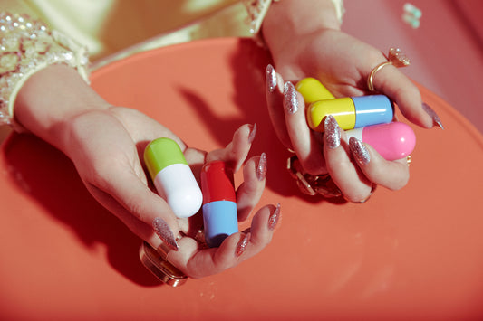 Female model girl with silver glitter nails manicure holding giant oversized colorful pills pharmaceutical drugs