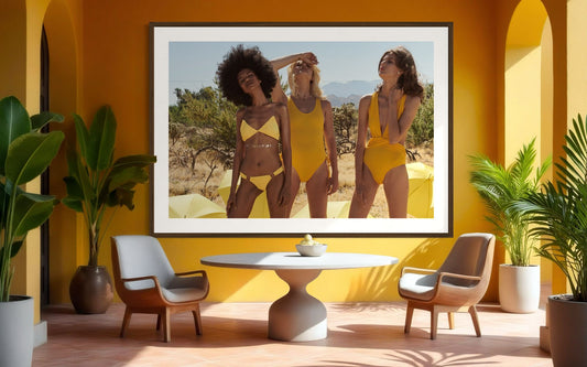 Framed photograph of three women in yellow swimsuits in a room with yellow walls, plants, and furniture.