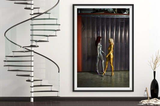 Framed artwork of two women walking down the street nude next to a modern spiral staircase.