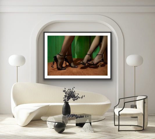 Modern living room with a framed artwork of feet, white sofa, glass coffee table, and black chairs.
