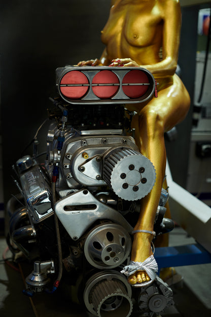 Gold nude painted Goldfinger bond girl in an auto body shop sitting on supercharger big block Chevy Engine.