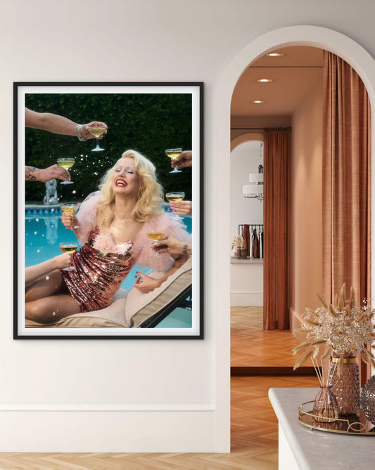 Framed artwork of a Amy Taylor lounging by a pool with six people serving her six glasses of champagne.