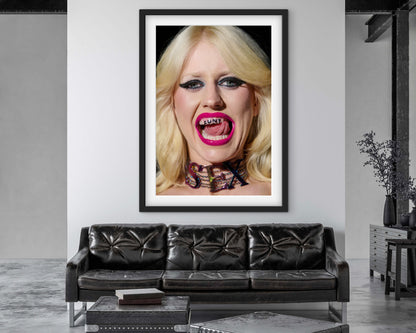 Punk woman Amy Taylor (Amyl and the Sniffers) wearing neon pink lipstick and licking her teeth that have 'CUNT' written on them.