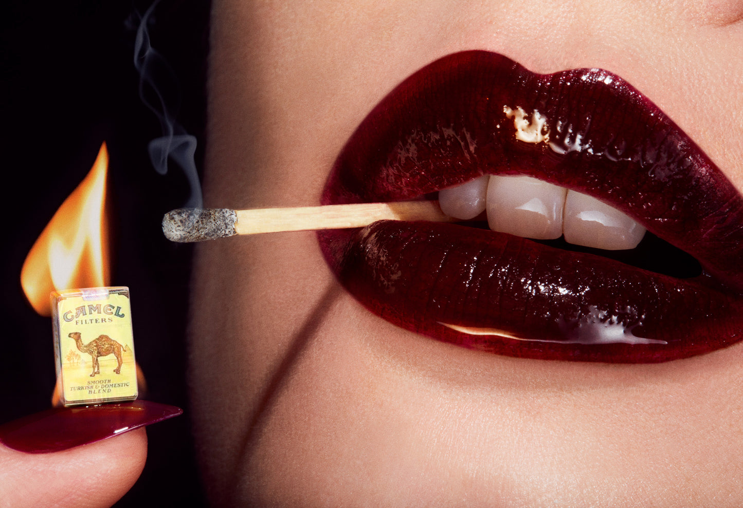 Woman with glossy burgundy lips with matchstick in her teeth lighting a miniature Camel cigarette pack on fire