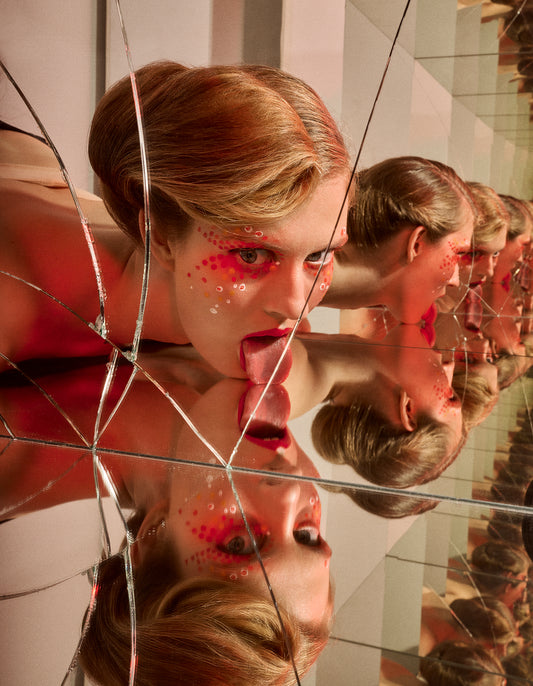 A creative artwork depicting a person with a bun hairdo looking into a cracked mirror with multiple reflections, with red avant garde makeup on the face.