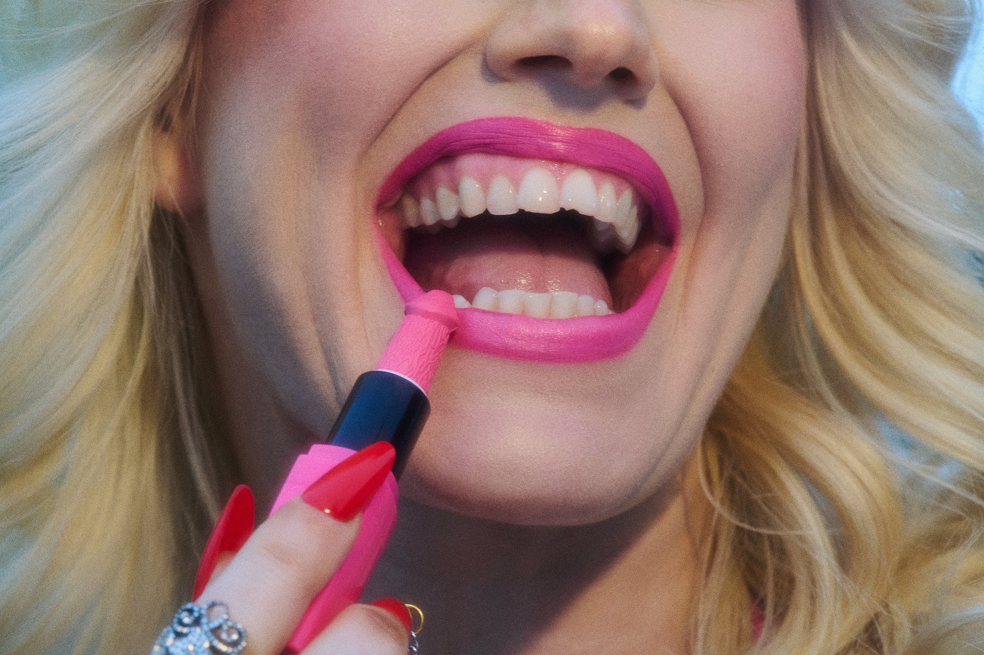 Close-up of blonde woman laughing while applying penis phallic pink lipstick.