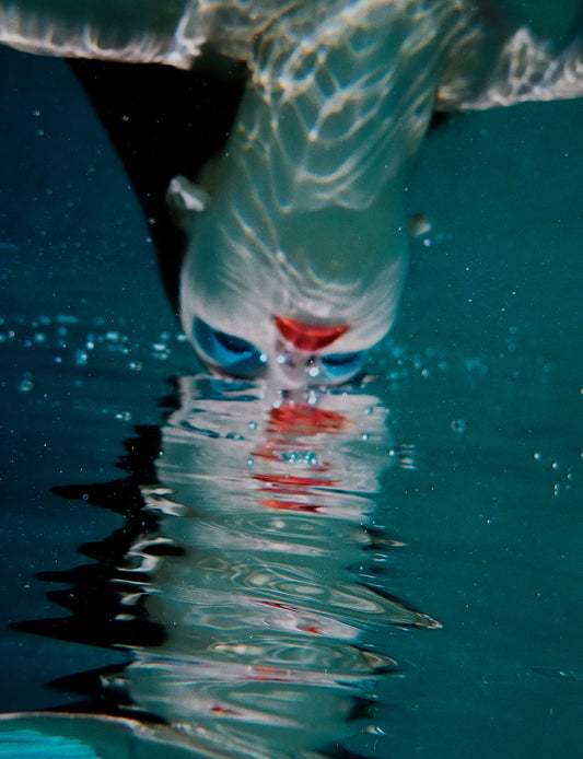 An underwater fine art photo print depicting a person with blue eyeshadow, partially submerged in water with air bubbles and a reflection on the surface.