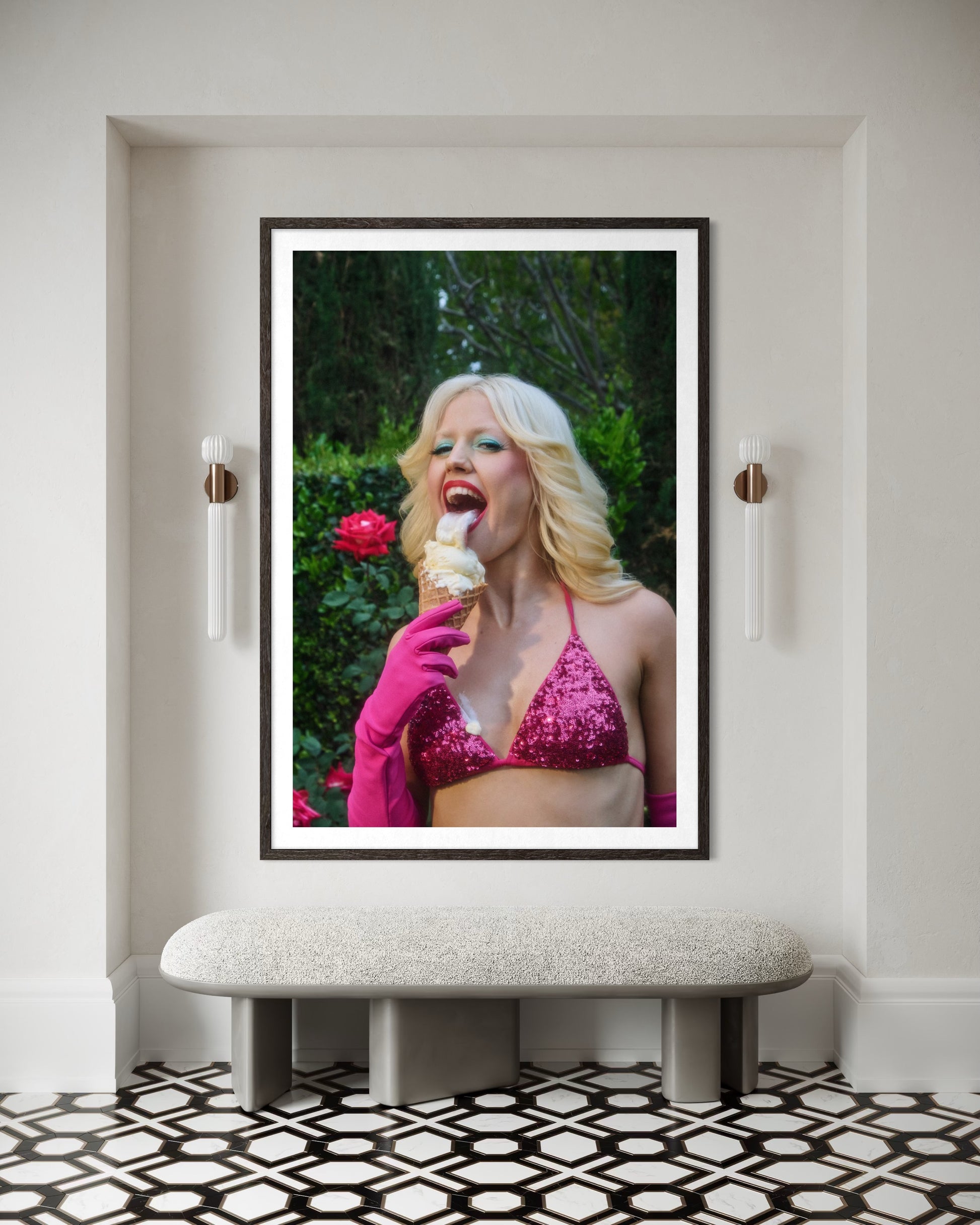 A fine art print of Amy Louise Taylor by Jamie Nelson. The punk singer of Amyl and the Sniffers has a blonde flip-out hairstyle and is wearing 80's style clothing and makeup—a pink bikini, gloves , blue eyeshadow, and red lipstick. She licks a messy ice cream cone with her big tongue as it drips onto her.