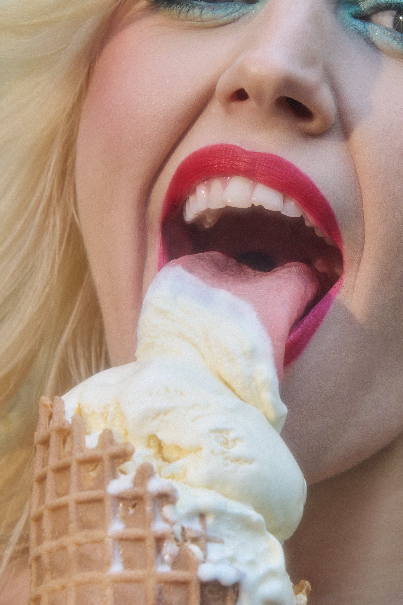 Close-up of woman licking ice cream with long tongue and wearing red lipstick and blue eyeshadow