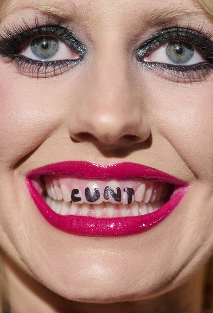 Close-up of a woman's face with 'CUNT' on her teeth.