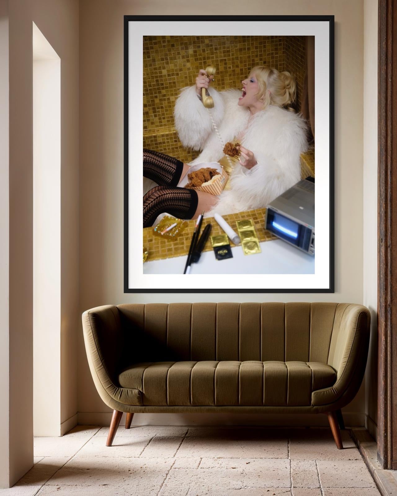 Framed artwork of Amy Taylor, of Amyl and the Sniffers, in a furry coat sitting inside a gold bath tub while yelling on the phone and eating fried chicken.